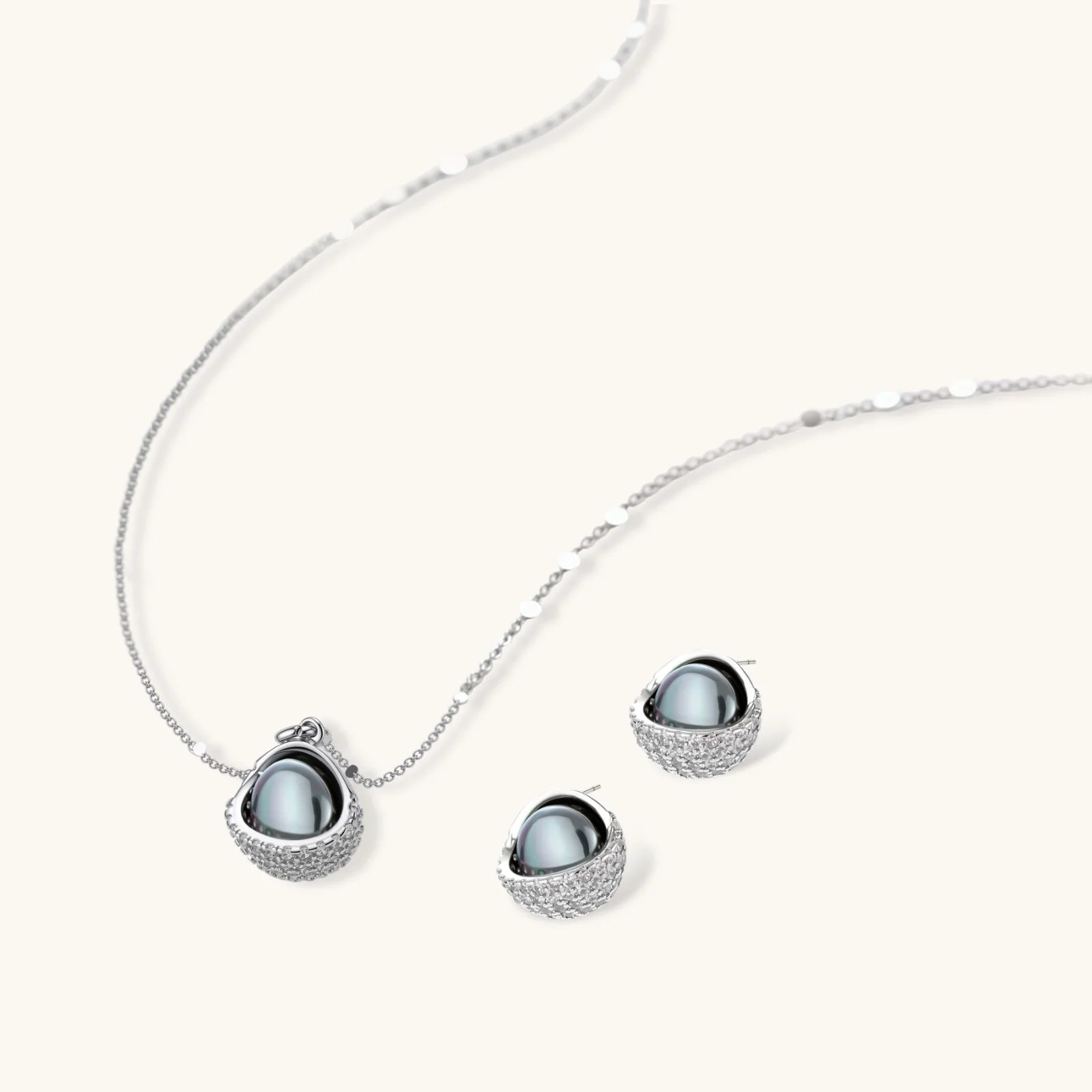 Elegant spherical pendant necklace and earrings set featuring crystal-pavé bottom half in gold or silver finish on white background.