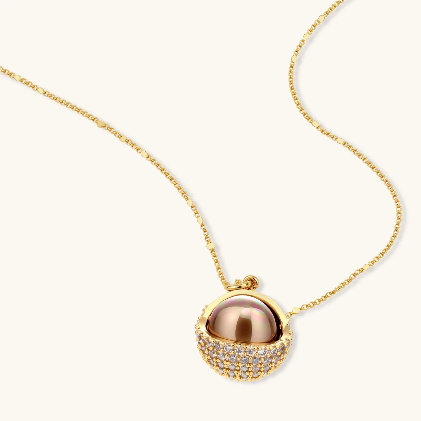 Elegant spherical pendant necklace and earrings set featuring crystal-pavé bottom half in gold or silver finish on white background.