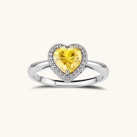 Heart-shaped yellow moissanite ring with diamond halo in sterling silver setting on neutral background