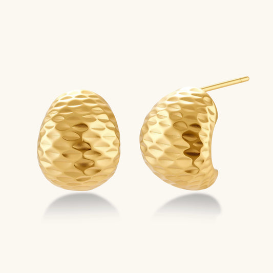 Pair of textured gold-plated sterling silver huggie earrings with dimpled surface finish on cream background.