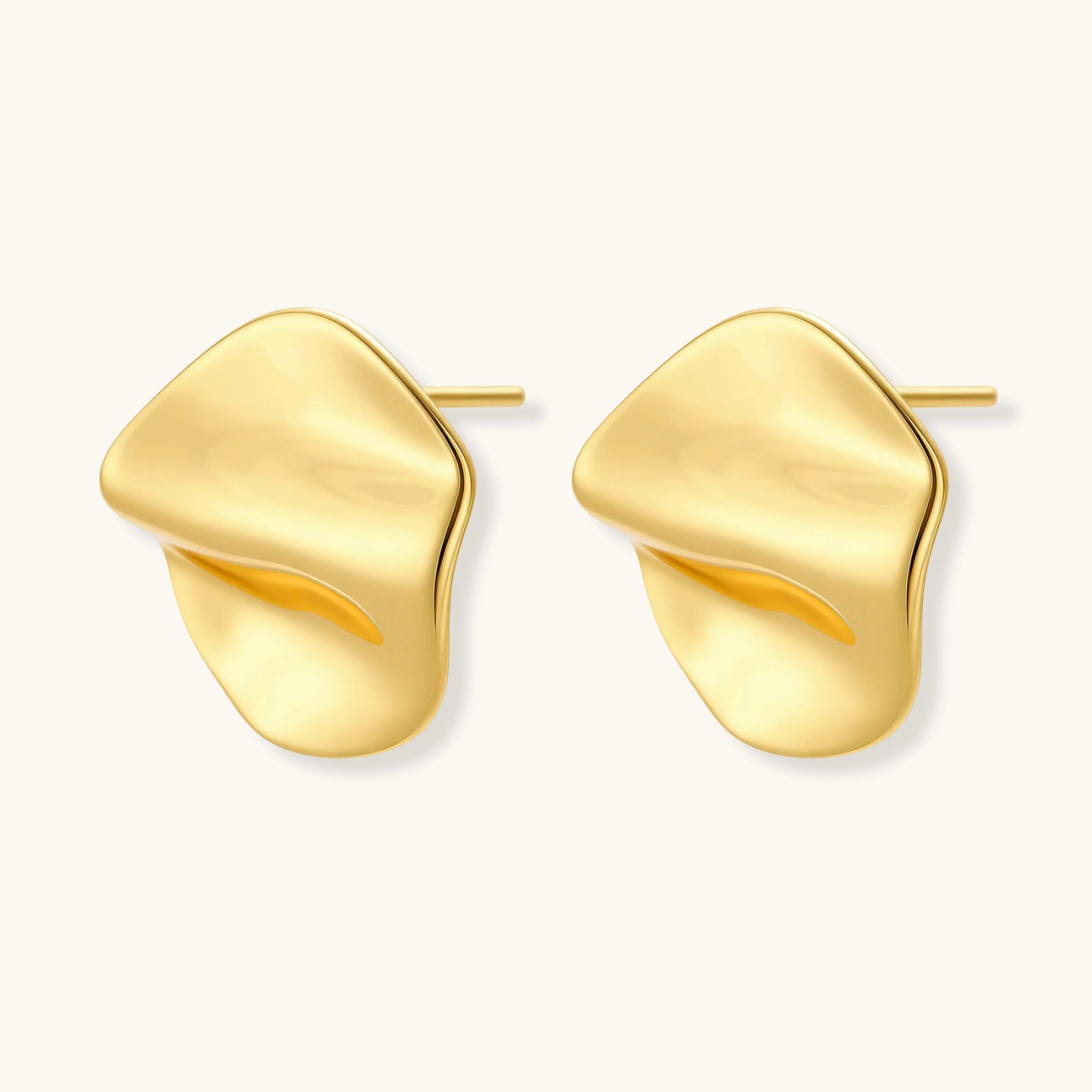Close-up of organic gold-plated sterling silver stud earrings with flowing sculptural design and curved cut-outs
