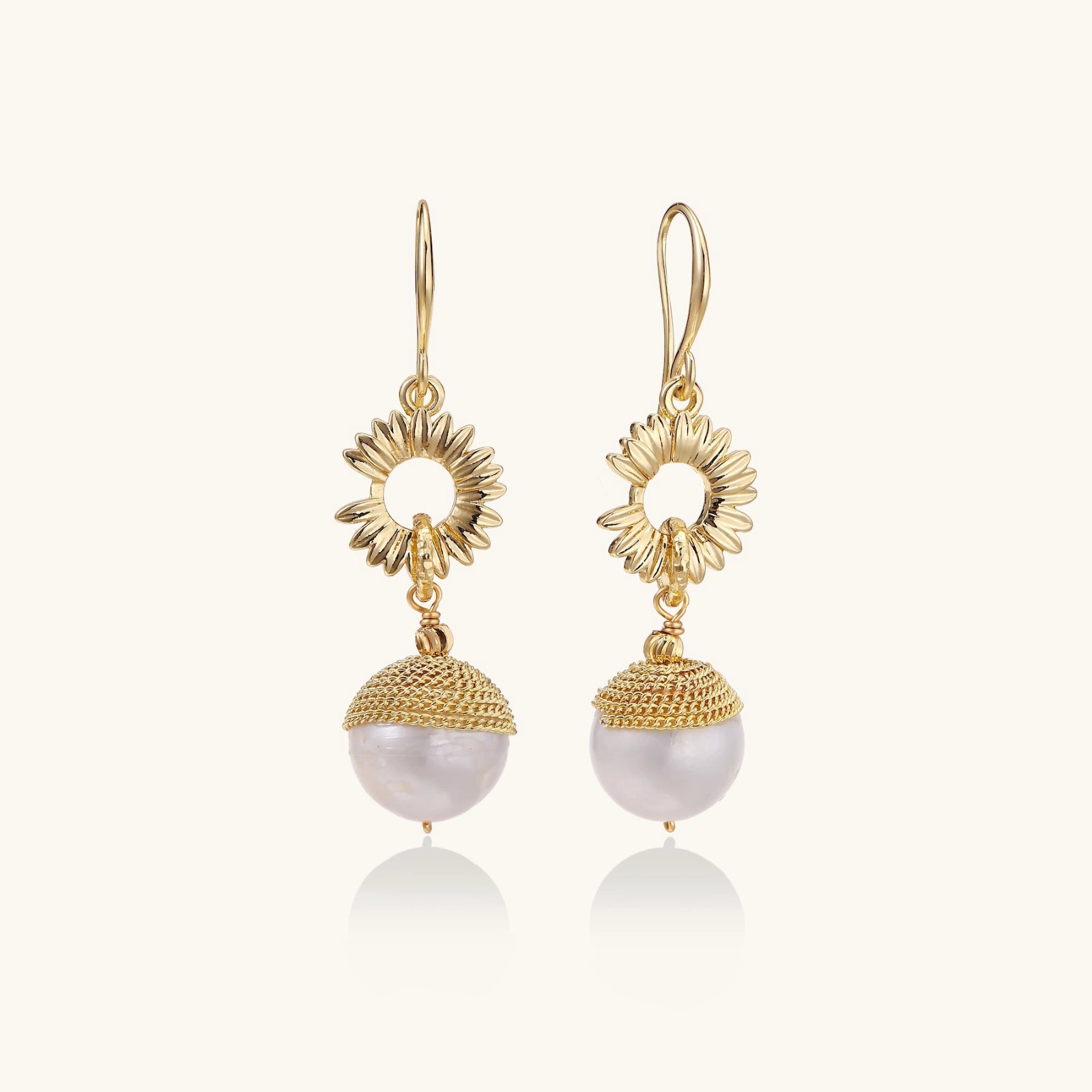 Gold sunburst charm earrings with baroque pearl drops on French hooks against cream background