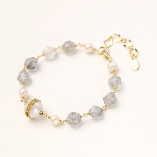 Bracelet with cloudy quartz beads, freshwater pearls, and gold-wrapped baroque pearl centerpiece on white background.