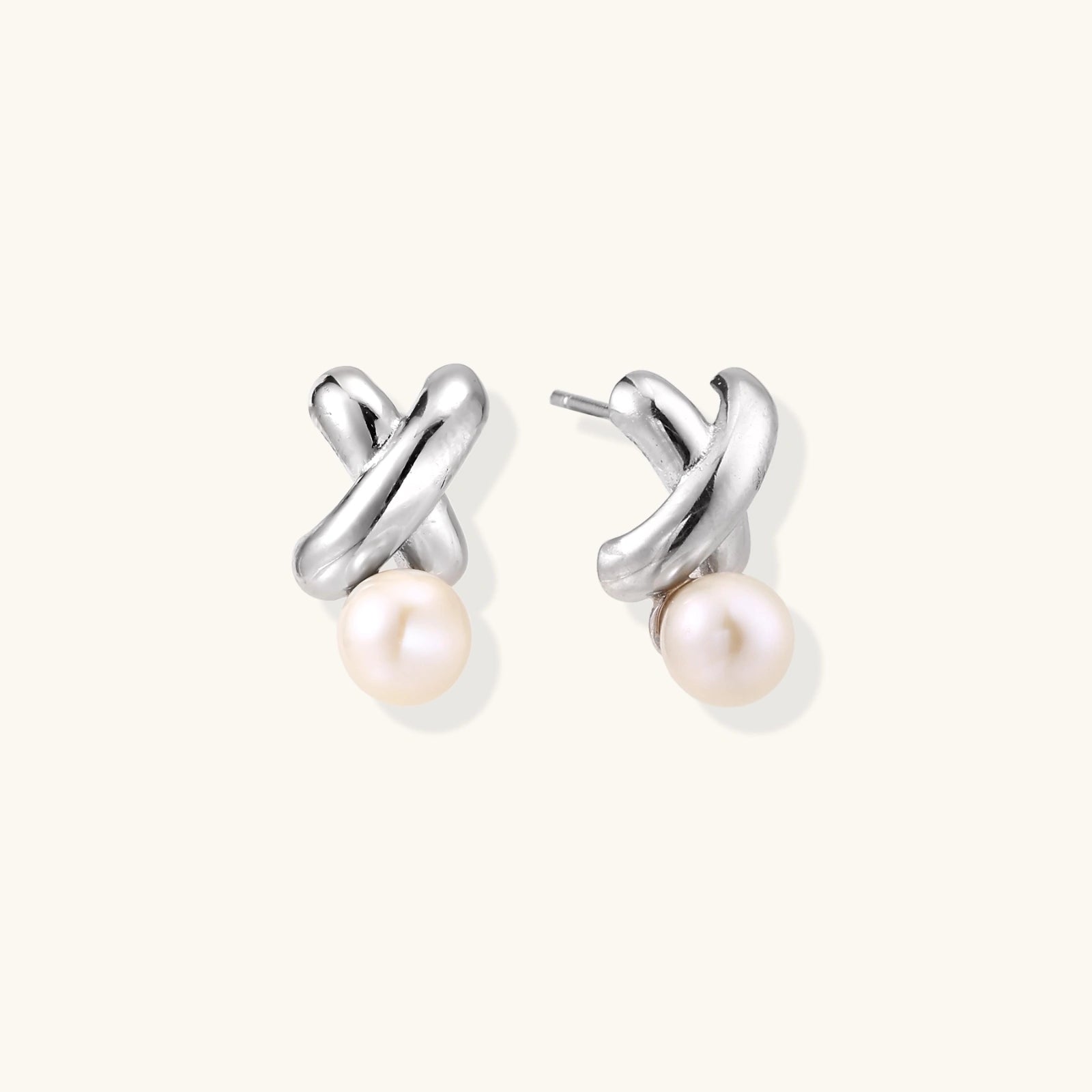 Rhodium-plated silver earrings with twisted X design and freshwater pearl drops on beige background