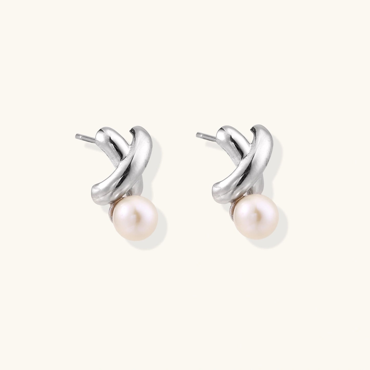 Rhodium-plated silver earrings with twisted X design and freshwater pearl drops on beige background