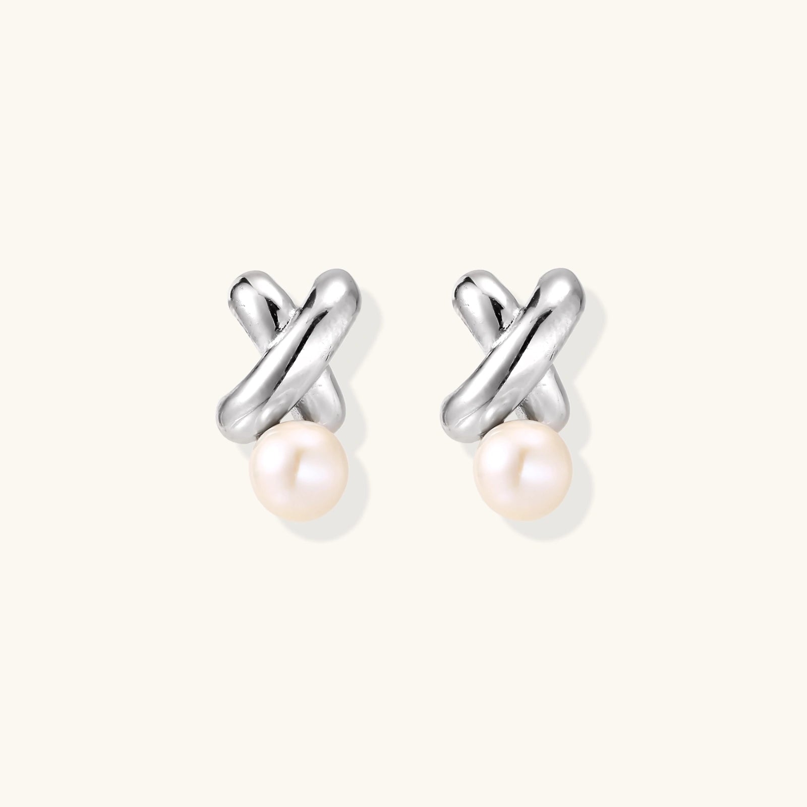 Rhodium-plated silver earrings with twisted X design and freshwater pearl drops on beige background