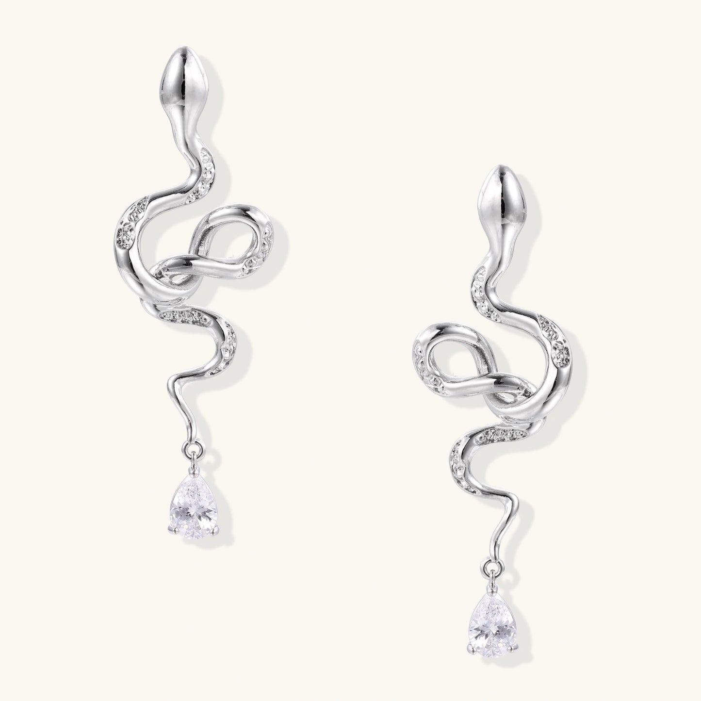 Silver snake-shaped drop earrings with crystal accents and teardrop stone dangles on cream background.
