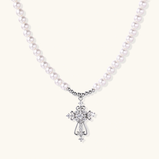 White pearl necklace with ornate silver cross pendant featuring zirconia crystals on cream background.