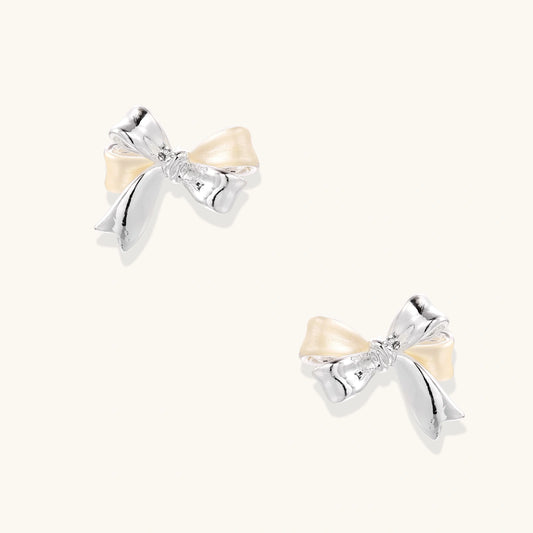 Dimensional bow stud earrings in white gold plated brass with silver and cream two-tone finish on neutral background