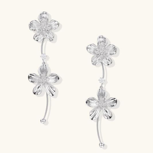 Silver-white asymmetric earrings with textured flower petals and crystal centers on cream background