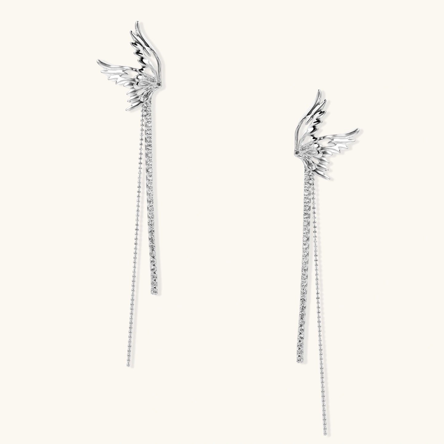 Pair of silver wing-shaped earrings with feather details and long sparkling crystal chain drops on cream background
