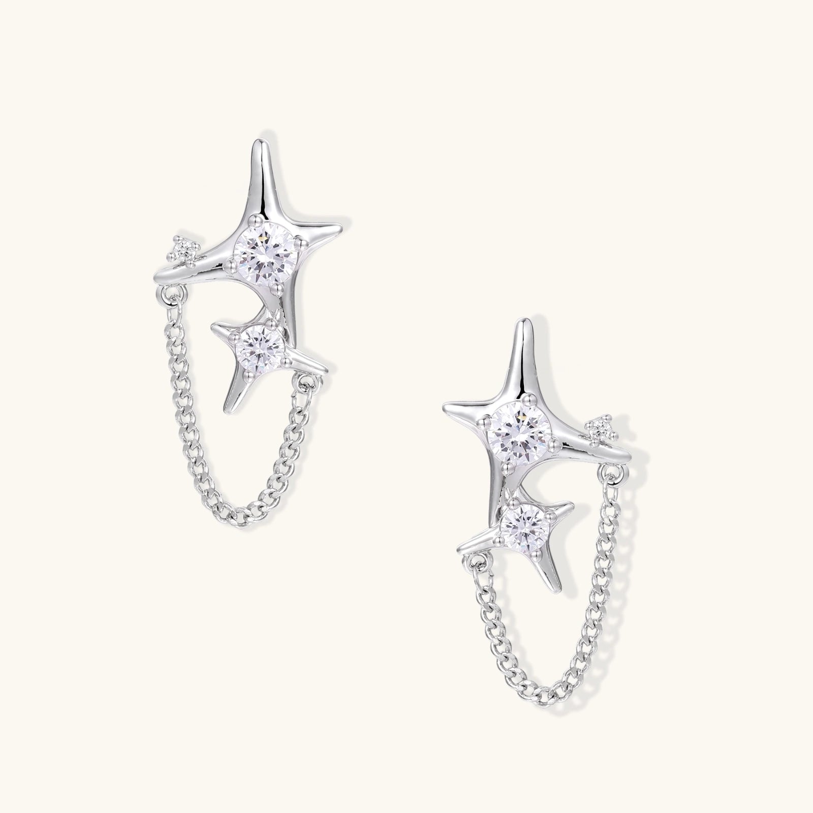 Silver star studs with crescent moon cutouts and zirconia stones connected by delicate chains on white background