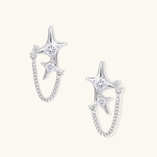 Silver star studs with crescent moon cutouts and zirconia stones connected by delicate chains on white background