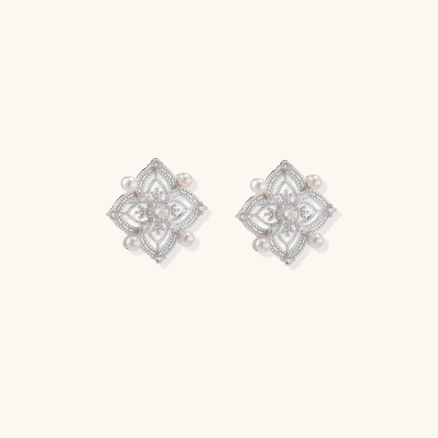 Ornate sterling silver stud earrings with mandala-inspired filigree pattern and four freshwater pearls on beige background
