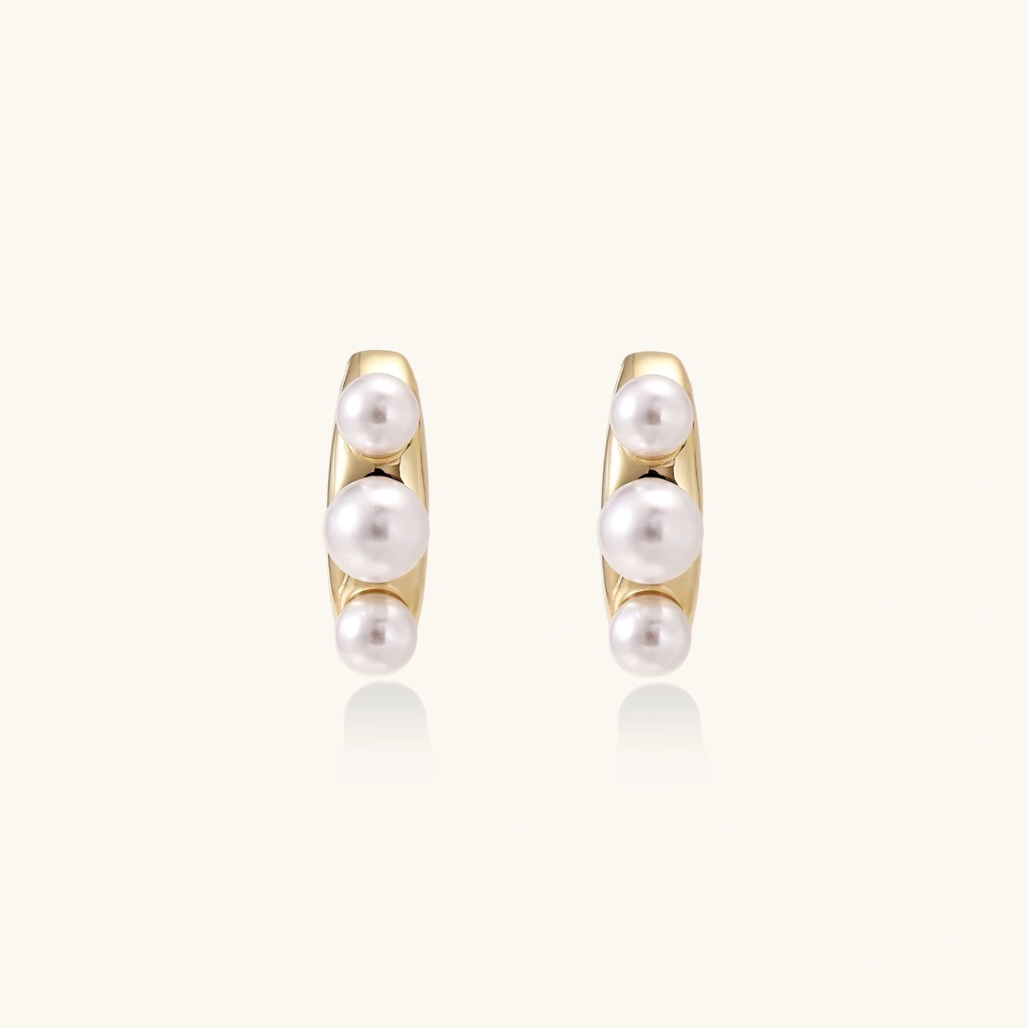 14K gold-plated curved stud earrings with three white freshwater pearls aligned vertically on cream background