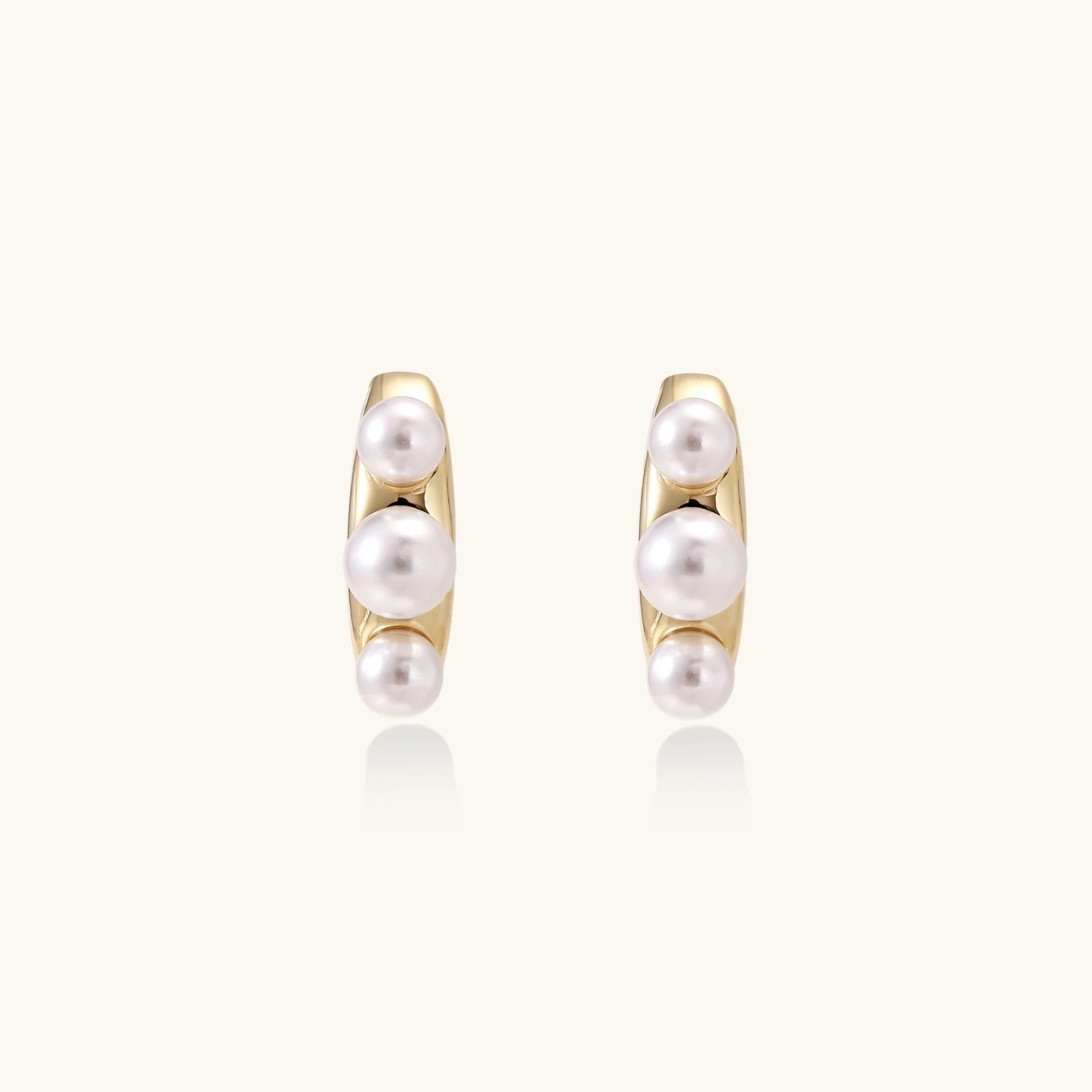 14K gold-plated curved stud earrings with three white freshwater pearls aligned vertically on cream background
