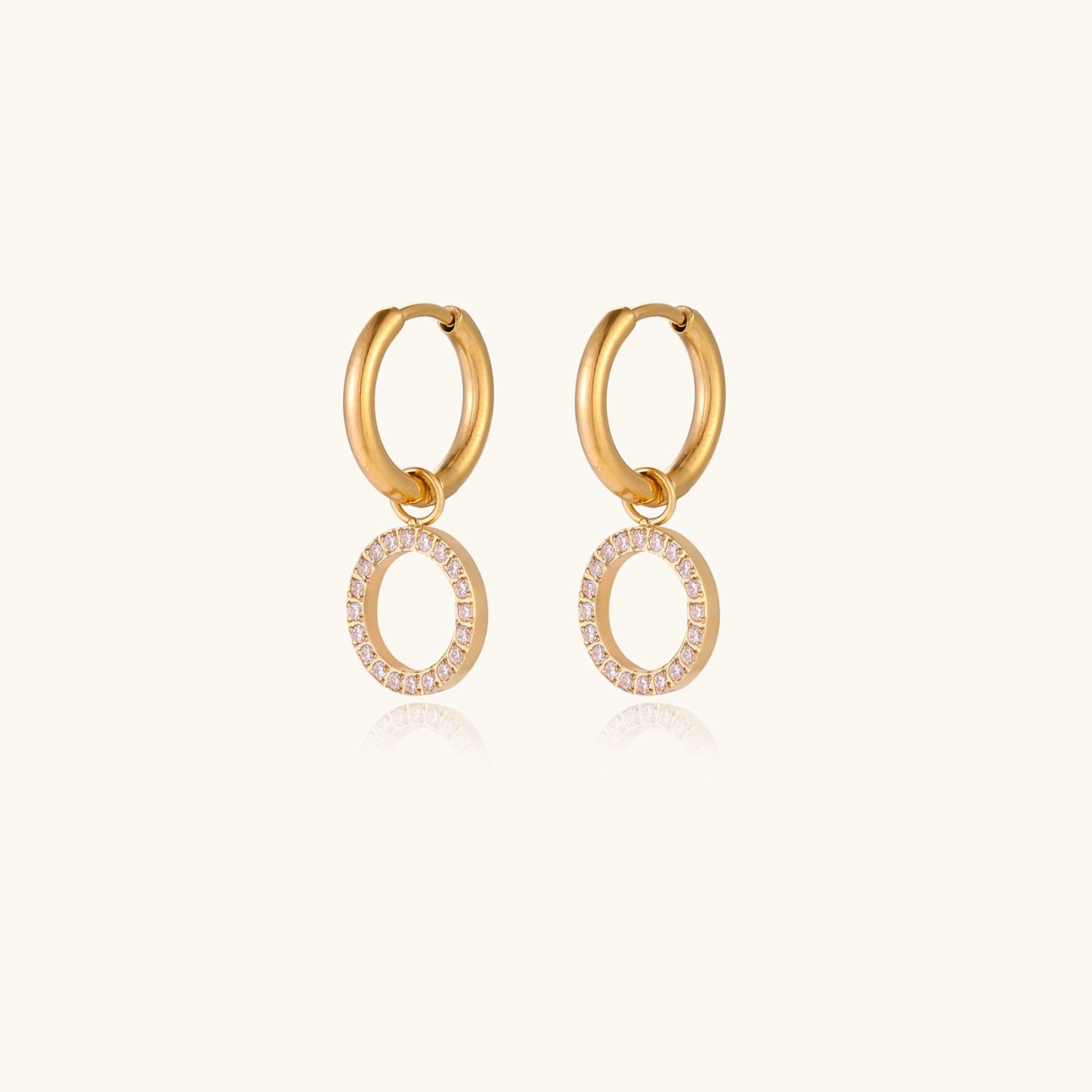 Gold-plated huggie hoop earrings with CZ-studded open circle charms on beige background