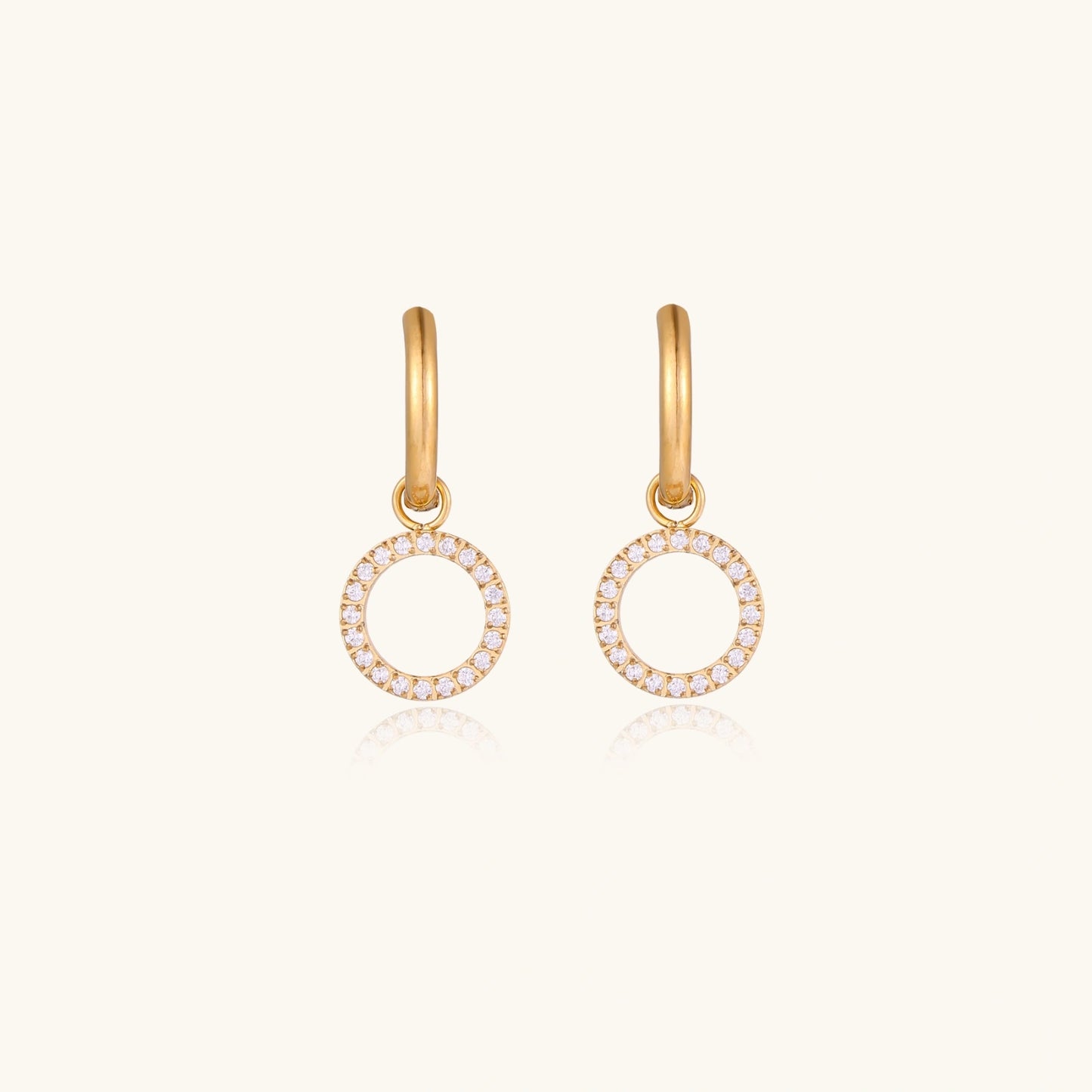 Gold-plated huggie hoop earrings with CZ-studded open circle charms on beige background