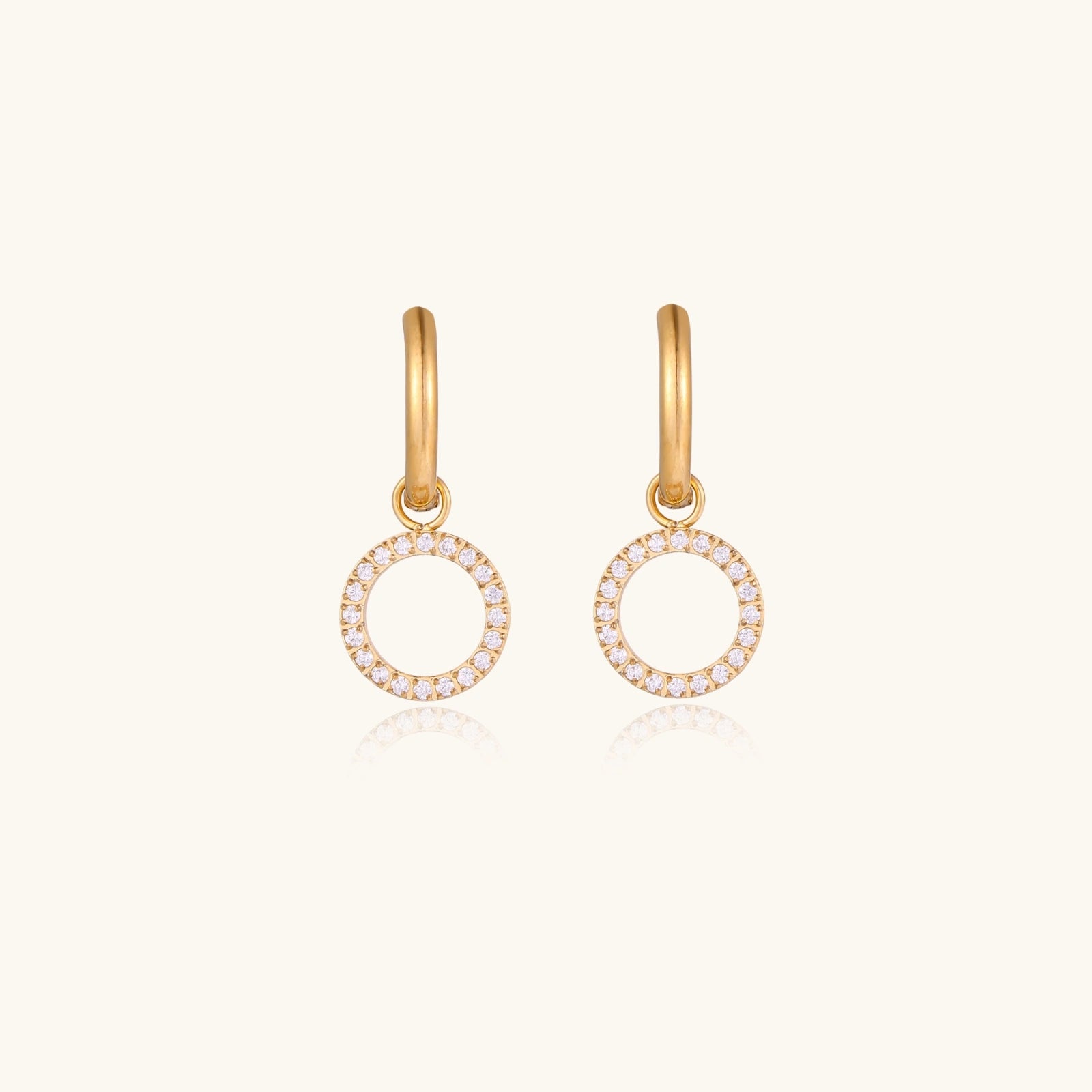 Gold-plated huggie hoop earrings with CZ-studded open circle charms on beige background