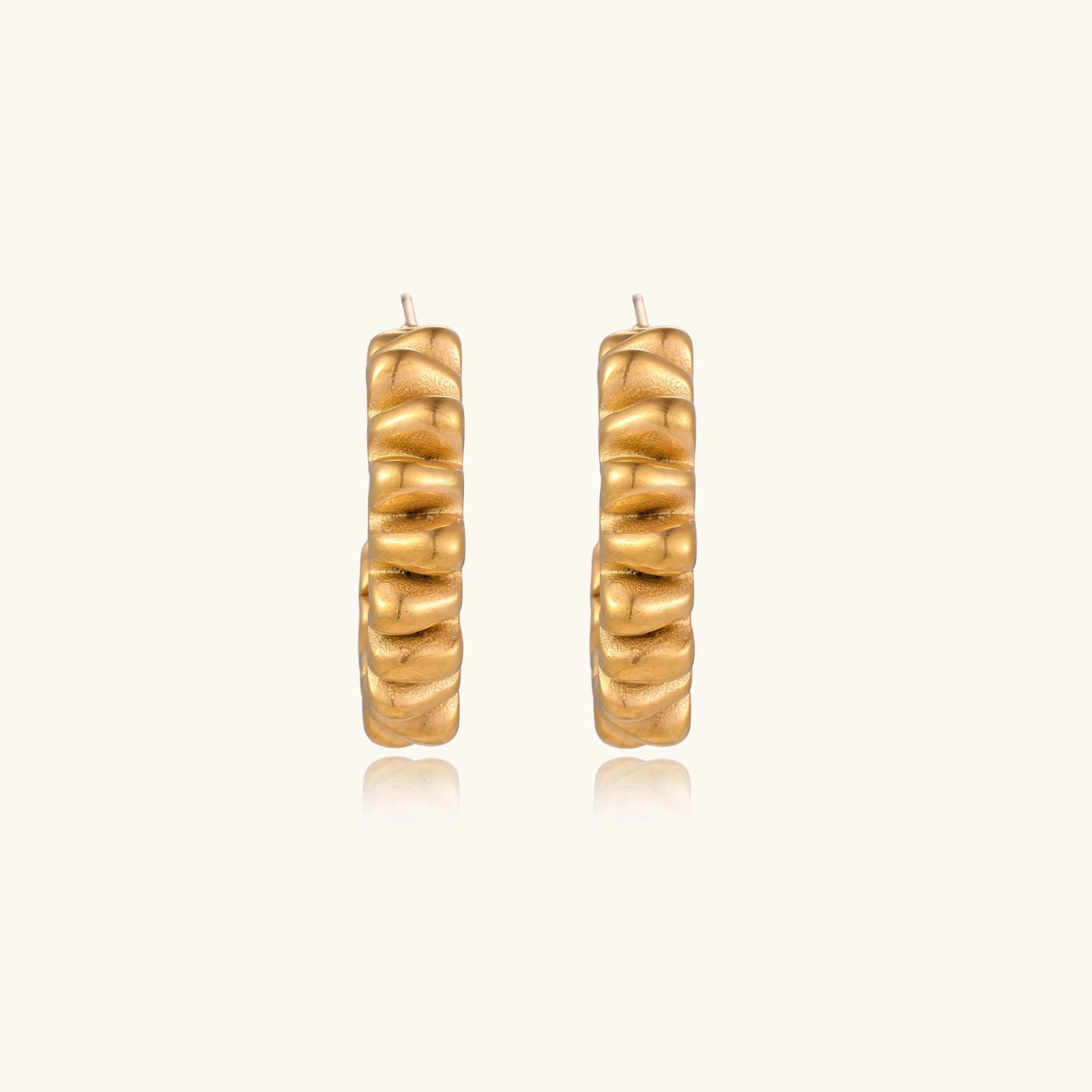 Sculptural gold-plated hoop earrings with continuous twisted spiral design on cream background