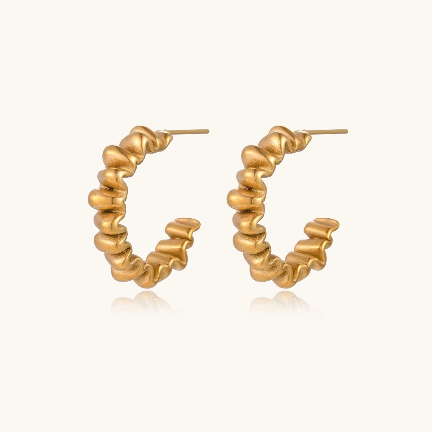 Sculptural gold-plated hoop earrings with continuous twisted spiral design on cream background