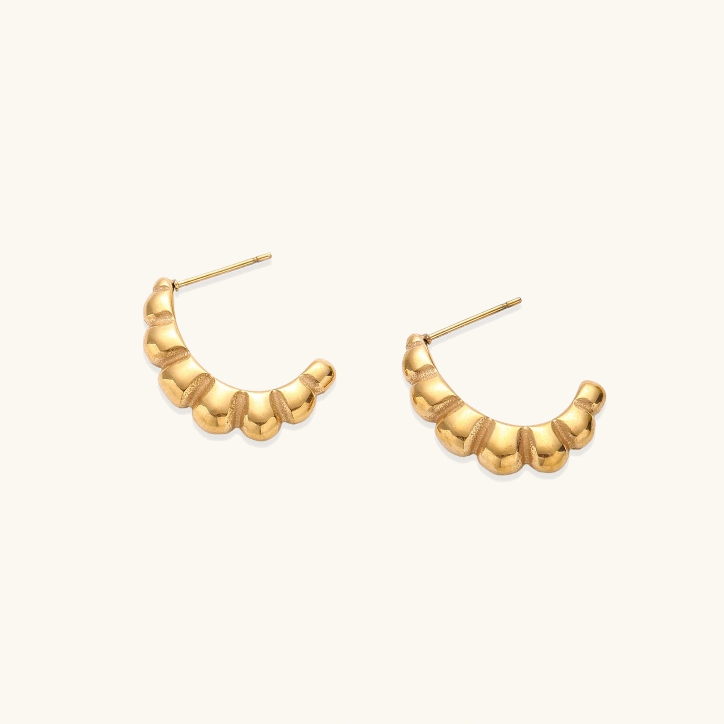 Gold-plated chunky hoop earrings with ridged bubble texture on cream background