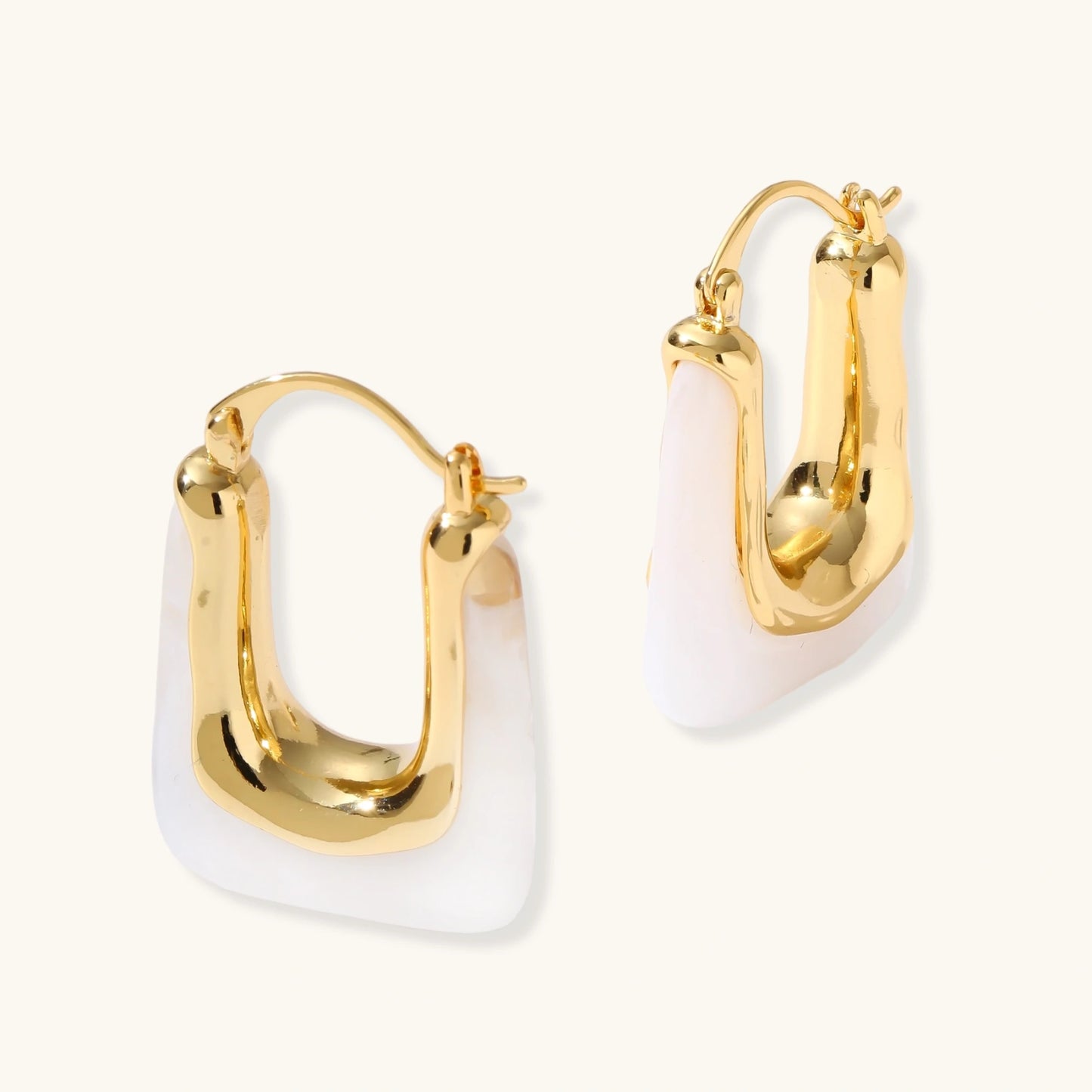 Sculptural gold-plated hoop earrings with flowing curved design and lever-back closure on cream background.