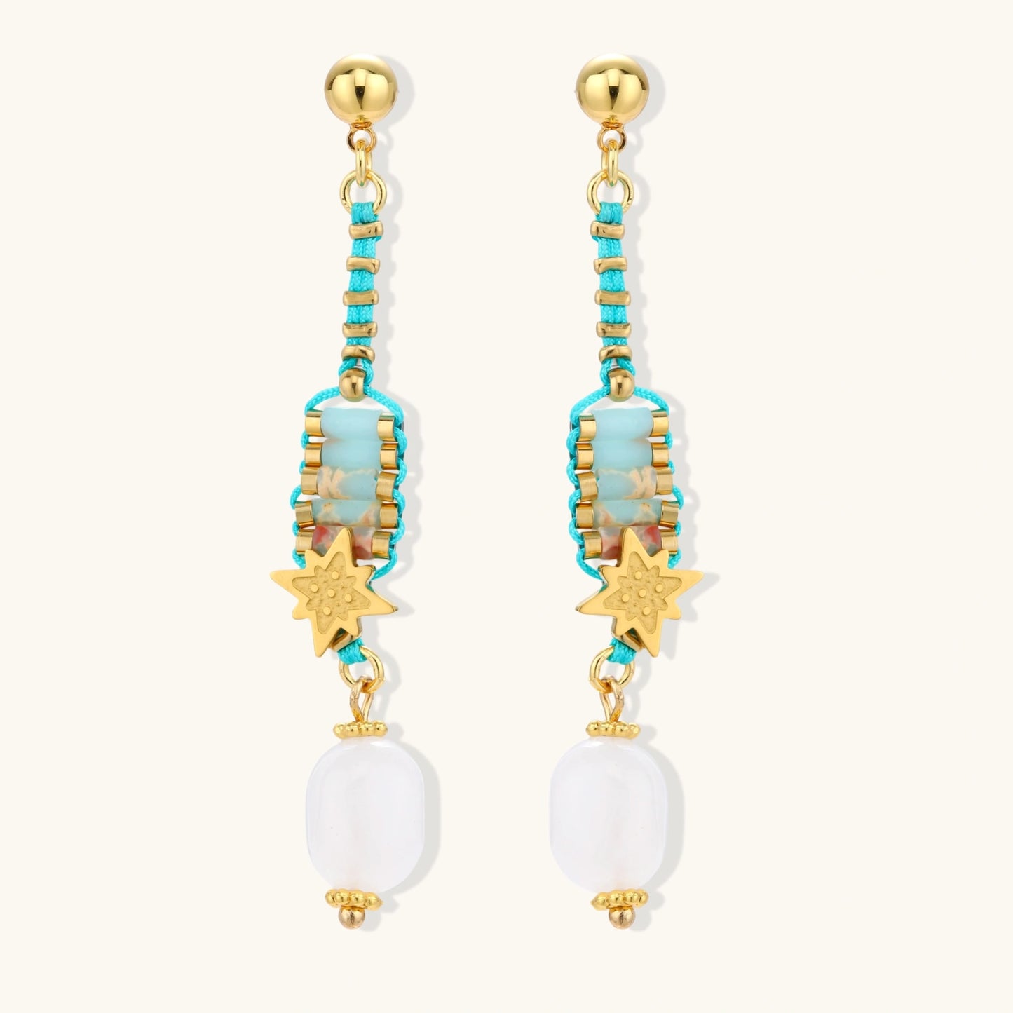 Gold-plated dangle earrings with turquoise threading, star charms, and white pearl beads against cream background.