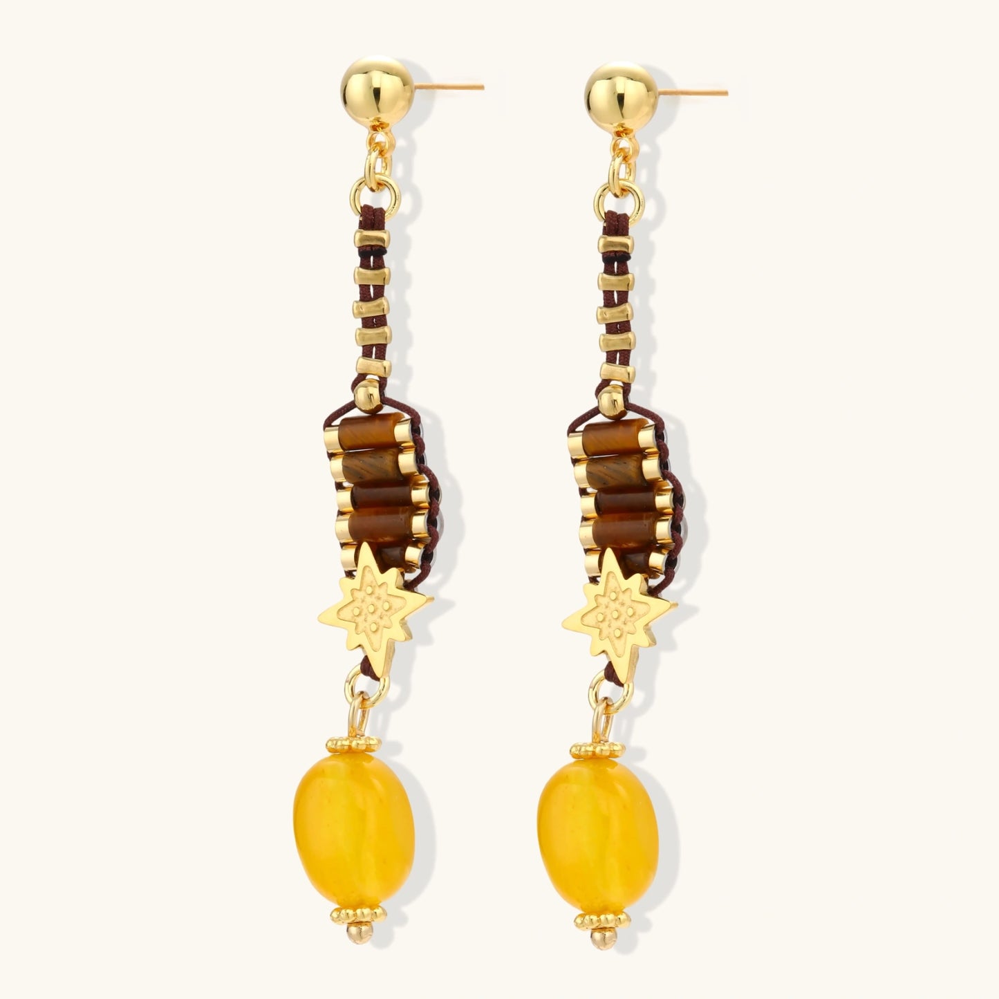Gold-plated dangle earrings with brown gemstones, star charms, and yellow amber drops on cream background.