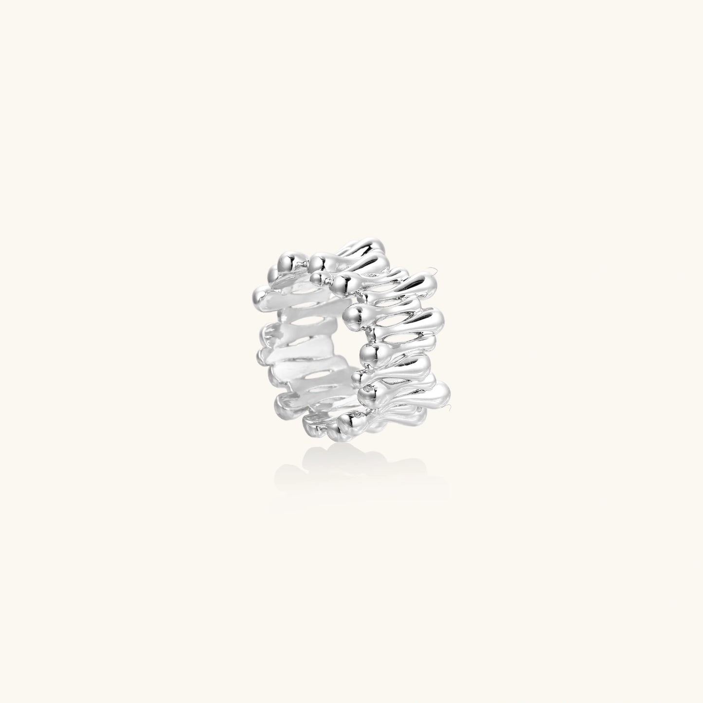 Wide band ring with sculptural wave ripples in polished white gold plated eco-brass on cream background